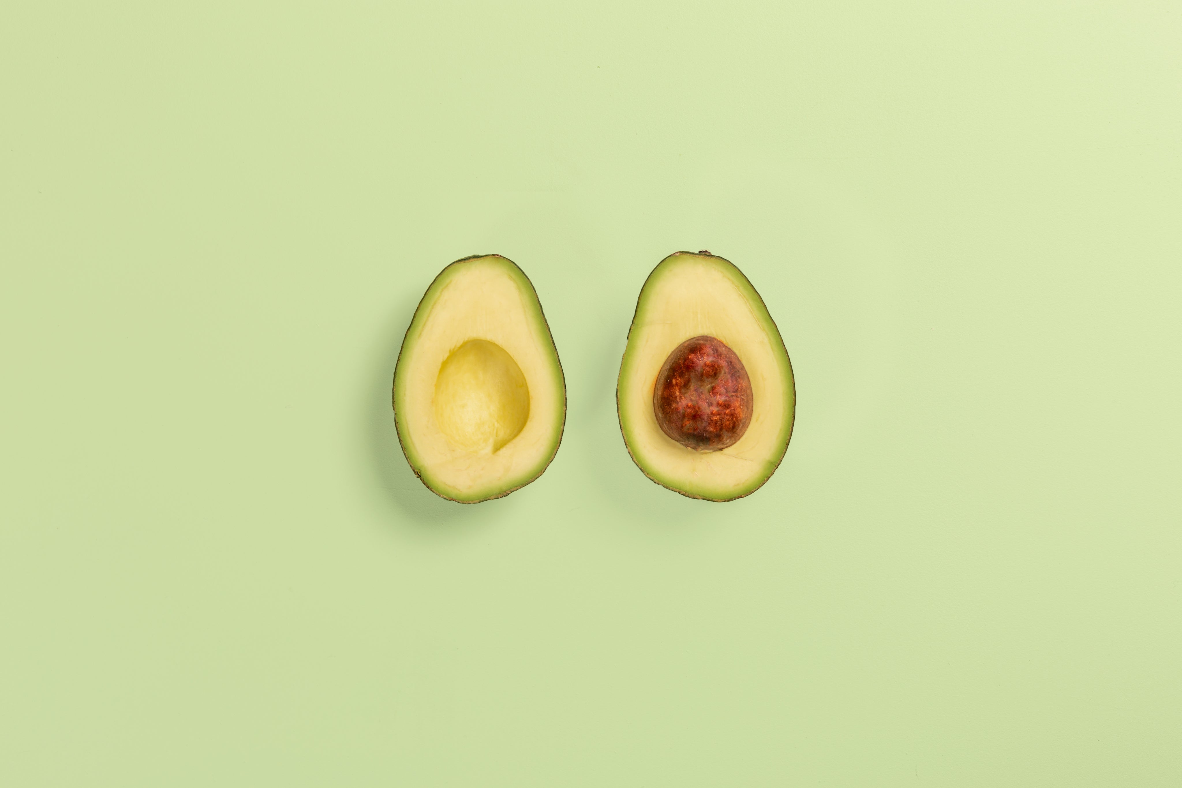Two avocado halves showing the green flesh and brown pit